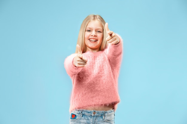 Feliz chica adolescente de pie, sonriendo aislado en estudio azul de moda.