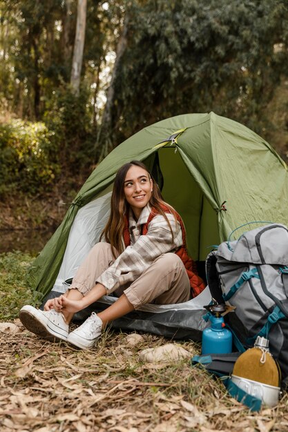 Feliz chica de camping en el bosque atando sus cordones vista larga