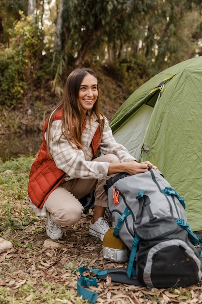 Feliz chica de camping en el bosque buscando la mochila