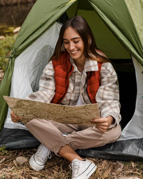 Feliz chica de camping en el bosque comprobando el mapa y sonrisas