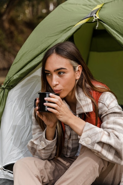 Feliz chica de camping en el bosque soplando en una taza