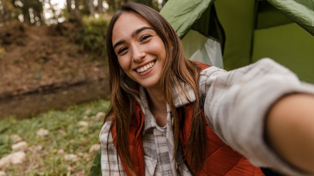 Feliz chica de camping en el bosque tomando una foto del uno mismo