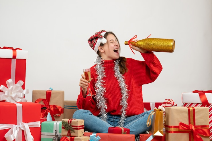 Foto gratuito feliz chica fiestera con gorro de papá noel bebiendo champán sentados alrededor presenta en blanco