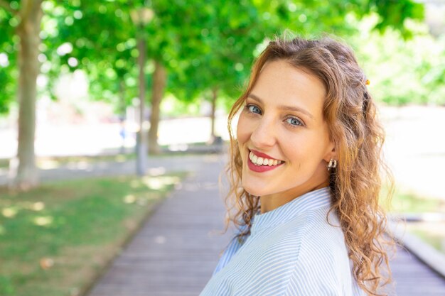 Feliz chica de pelo ondulado sonriendo a la cámara al aire libre