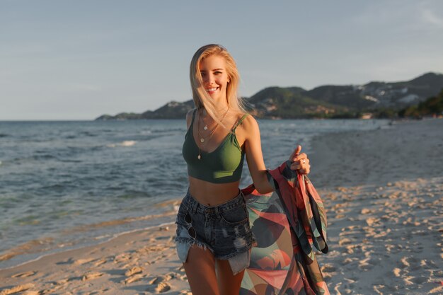 Feliz chica rubia corriendo en la playa, disfrutando el verano.