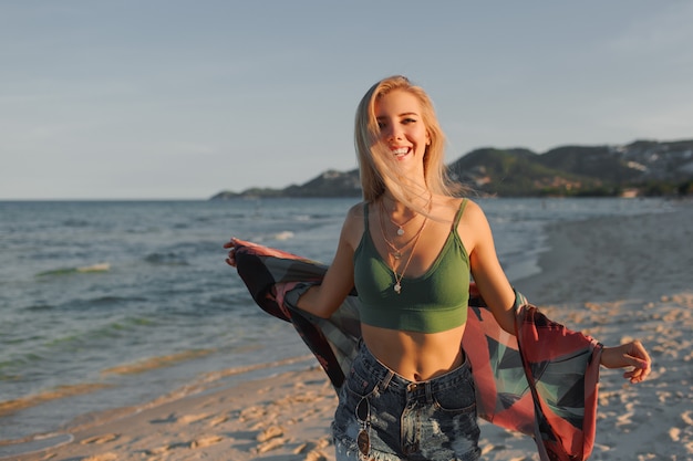 Feliz chica rubia corriendo en la playa, disfrutando el verano.