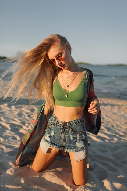 Feliz chica rubia posando en la playa, disfrutando el verano.