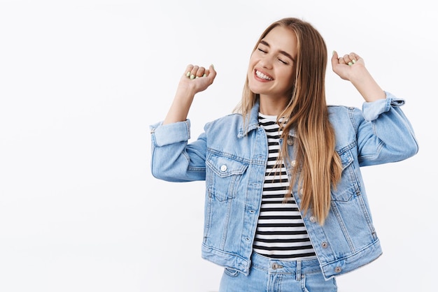 Feliz y complacida alegre chica rubia celebrando la victoria sonriendo alegremente con los ojos cerrados expresión encantada levanta las manos levantando el puño con alegría celebrando ganar grandes noticias convertirse en campeón