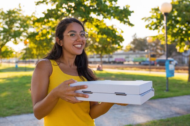 Feliz correo femenino latino llevando pizza en el parque