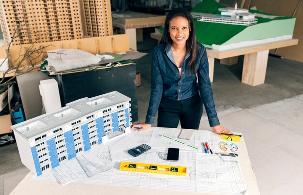 Feliz dama afroamericana de pie cerca del modelo de edificio en mesa