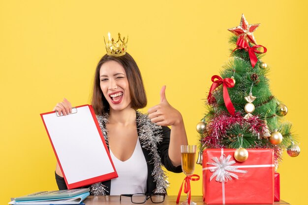 Feliz dama encantadora en traje con corona con documento en la oficina