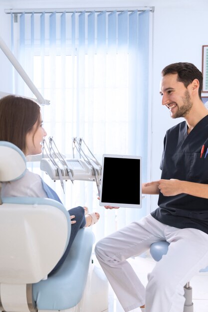 Feliz dentista apuntando en la pantalla de la tableta digital a paciente femenino en la clínica