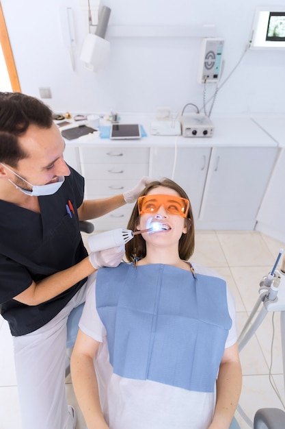Feliz dentista masculino comprobar los dientes del paciente con equipos de luz UV dental en la clínica