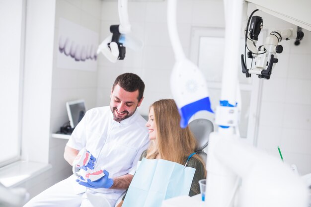 Feliz dentista masculino mostrando el modelo de los dientes al paciente