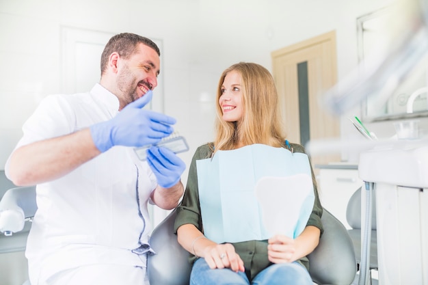 Feliz dentista y paciente mirando el uno al otro mientras elige el tono de color de sus dientes