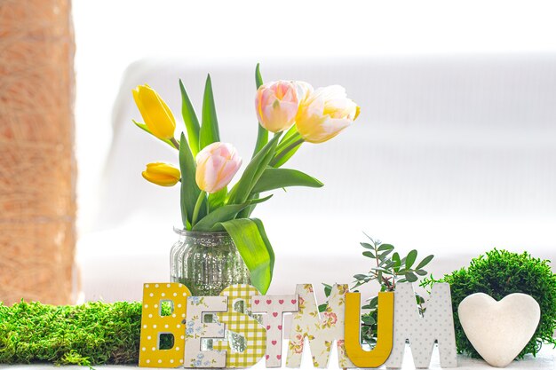 Feliz día de la madre. Letras sobre un fondo blanco. Inscripción de madera para el día de la madre en una mesa de madera en la sala de estar con un hermoso ramo de tulipanes de primavera.