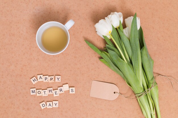 Feliz día de la madre texto; Té de limón con flores de tulipán blanco sobre fondo marrón