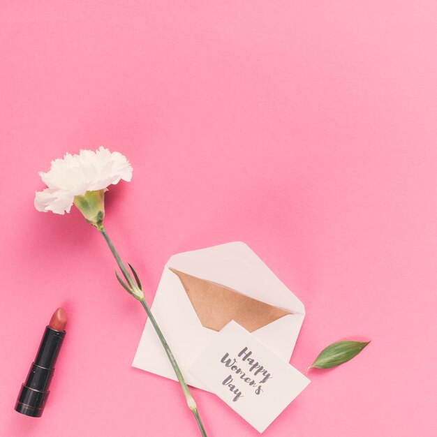 Feliz día de la mujer inscripción con sobre y flor en mesa rosa