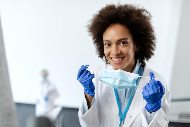 Feliz doctora negra usando mascarilla protectora y mirando a la cámara