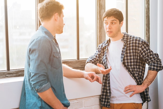 Feliz dos amigo masculino de pie cerca de la ventana gesticulando