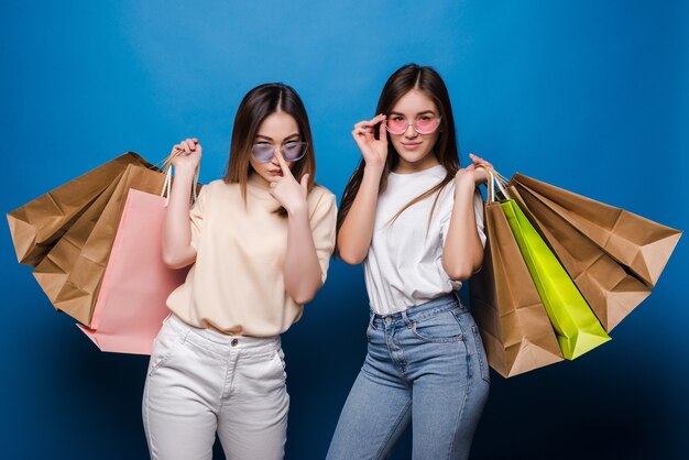 Feliz dos mujeres con coloridas bolsas de la compra en la pared azul