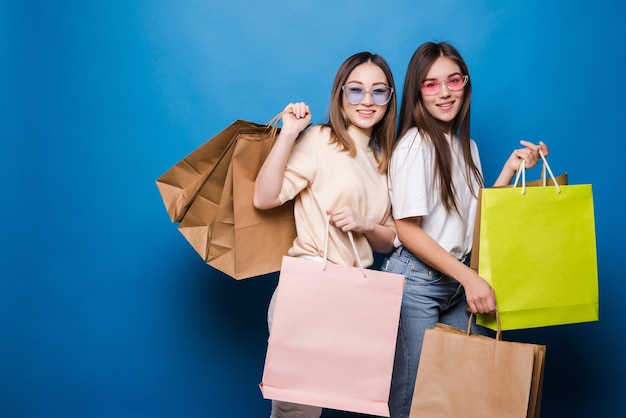 Feliz dos mujeres con coloridas bolsas de la compra en la pared azul