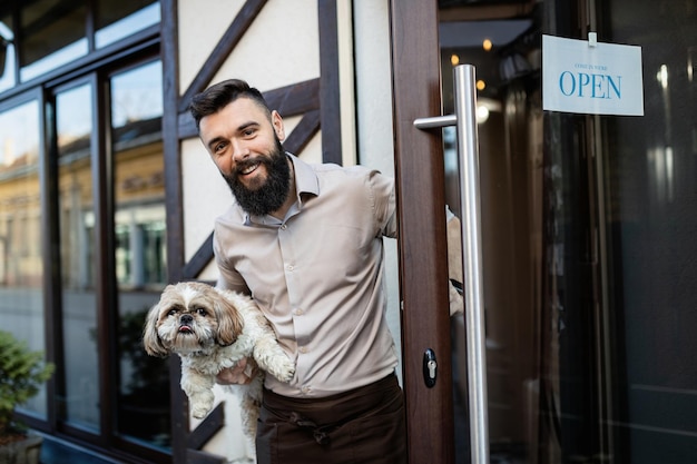 Feliz dueño del bar sosteniendo a un perro mientras abre la puerta de entrada y mira la cámara