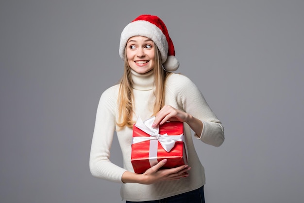 Feliz emocionada joven con sombrero de santa claus con caja de regalo aislada sobre pared gris