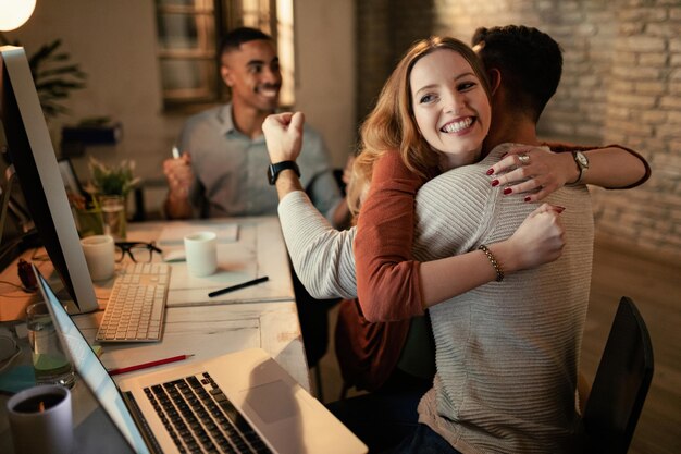 Feliz empresaria abrazando a su compañero de trabajo mientras celebra el éxito en la oficina