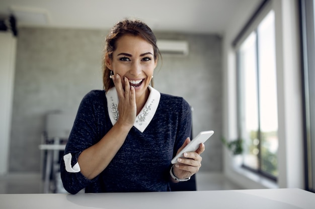 Feliz empresaria leyendo un mensaje de texto con incredulidad en la oficina