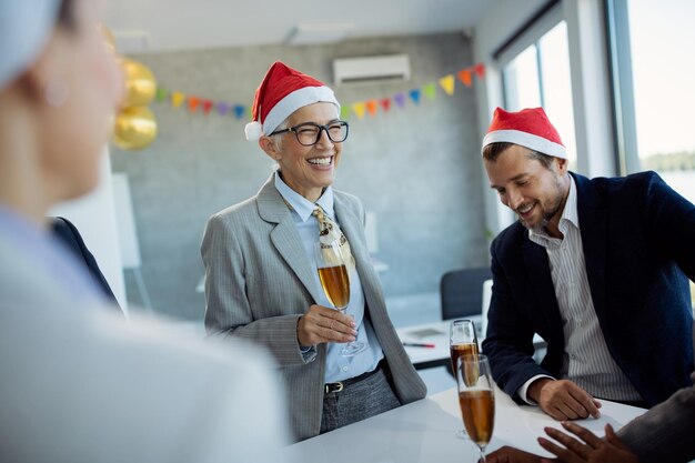 Feliz empresaria madura con una copa de champán en la fiesta de Navidad en la oficina