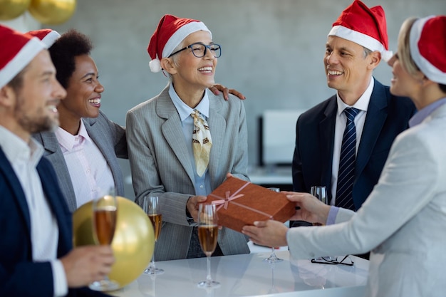 Feliz empresaria madura recibiendo un regalo de sus colegas en la fiesta de Navidad en la oficina