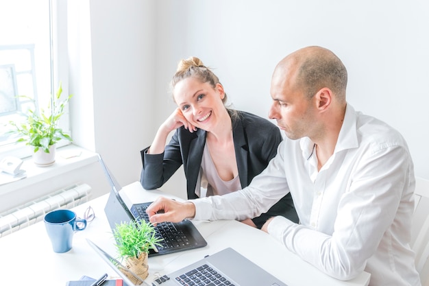 Feliz empresaria sentado con su colega trabajando en la computadora portátil