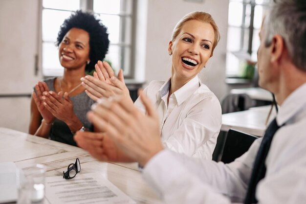 Feliz empresaria y sus compañeros de trabajo aplaudiendo en una reunión en la oficina