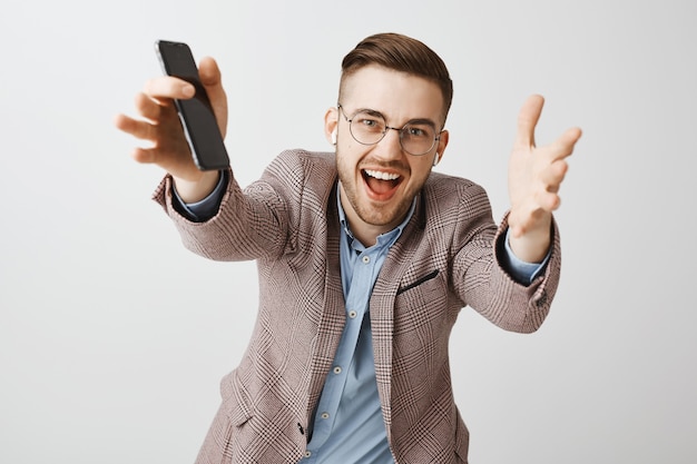 Feliz empresario masculino guapo extendiendo las manos hacia adelante, escuchando música con auriculares inalámbricos y lista de reproducción en la aplicación de teléfono móvil