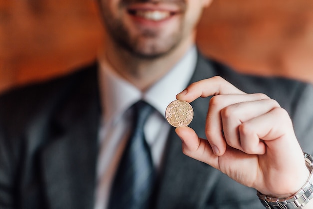 Foto gratuita feliz empresario tiene un bitcoin en una mano en la pared naranja