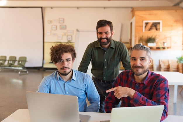 Feliz equipo exitoso de inicio con computadoras portátiles posando en la sala de juntas