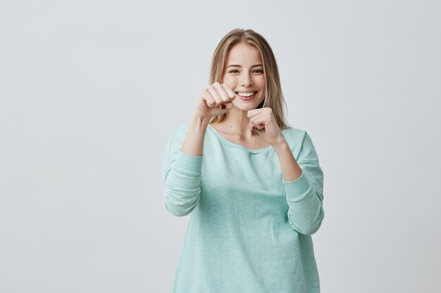 feliz exitosa joven rubia ganadora vestida casualmente manteniendo los puños cerrados mientras anima y se siente afortunado