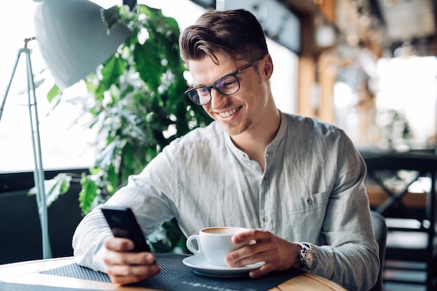 Feliz exitoso hombre en anteojos, usando teléfono celular, sonriendo alegremente