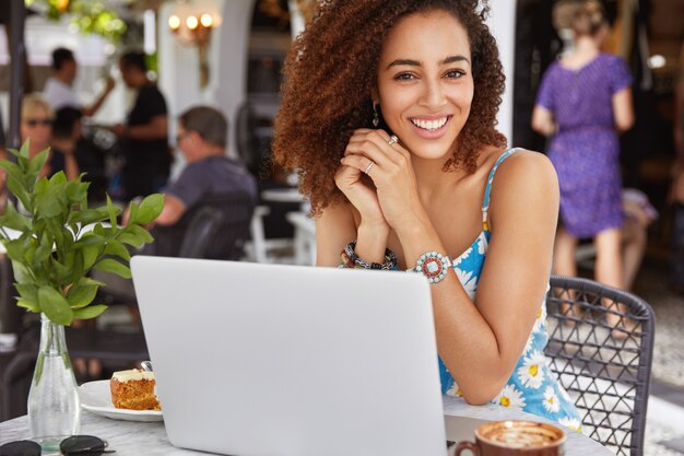 Feliz exitoso y talentoso joven redactora afroamericana trabaja en una computadora portátil en el restaurante