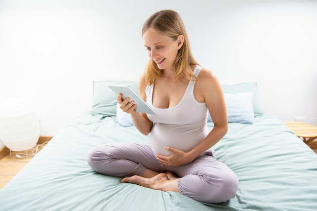 Feliz expectante mamá leyendo en la pantalla de la tableta