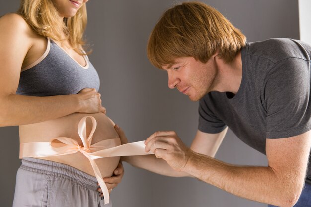 Feliz expectante papá desatando la cinta en el vientre de la esposa embarazada