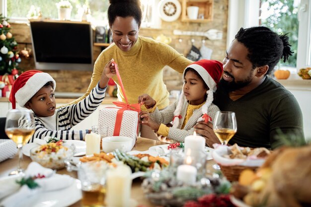 Feliz familia afroamericana abriendo regalos de Navidad en la mesa de comedor