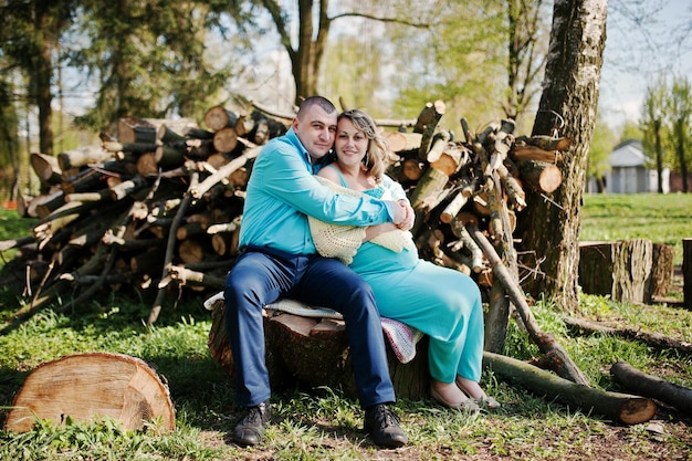 Feliz familia embarazada vestida con ropa turquesa sentada en un tocón en el parque
