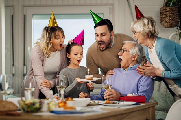 Feliz familia extendida soplando velas de cumpleaños en un pastel mientras celebra en el comedor