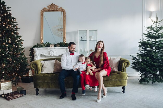 Feliz familia festiva sonriendo posando en el interior de vacaciones de diciembre de lujo en el fondo del árbol de Navidad