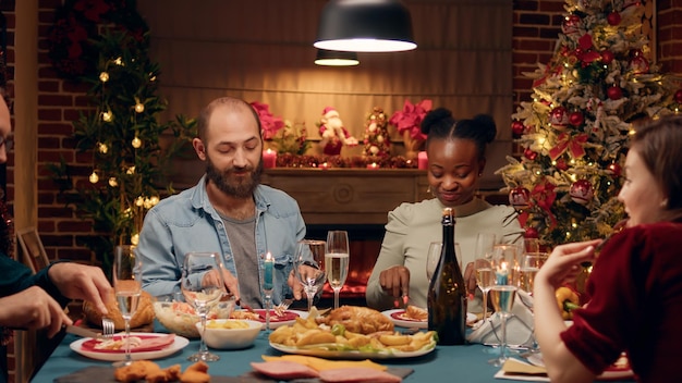Feliz familia multiétnica reunida alrededor de la mesa de la cena de Navidad disfrutando de comida casera tradicional. Parientes festivos sentados en casa mientras celebran juntos las vacaciones de invierno.