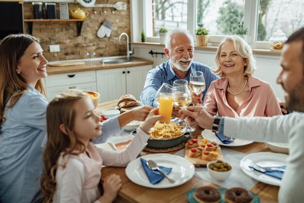 Feliz familia multigeneracional almorzando y brindando en la mesa de comedor El foco está en el hombre mayor