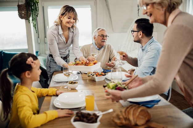 Feliz familia multigeneracional almorzando juntos en casa Los hombres hablan entre ellos mientras las mujeres sirven comida en la mesa del comedor