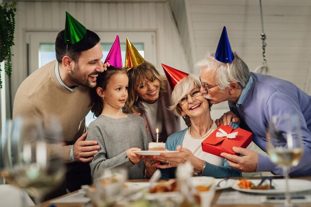 Feliz familia multigeneracional celebrando el cumpleaños de la abuela y sorprendiéndola con pastel de cumpleaños y regalos